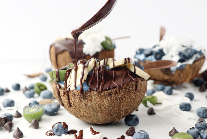 Drizzling Organic Keto Chocolate Over Chocolate Coconut Smoothie Bowls With Blueberries And Vegan Chocolate Chips From Pascha