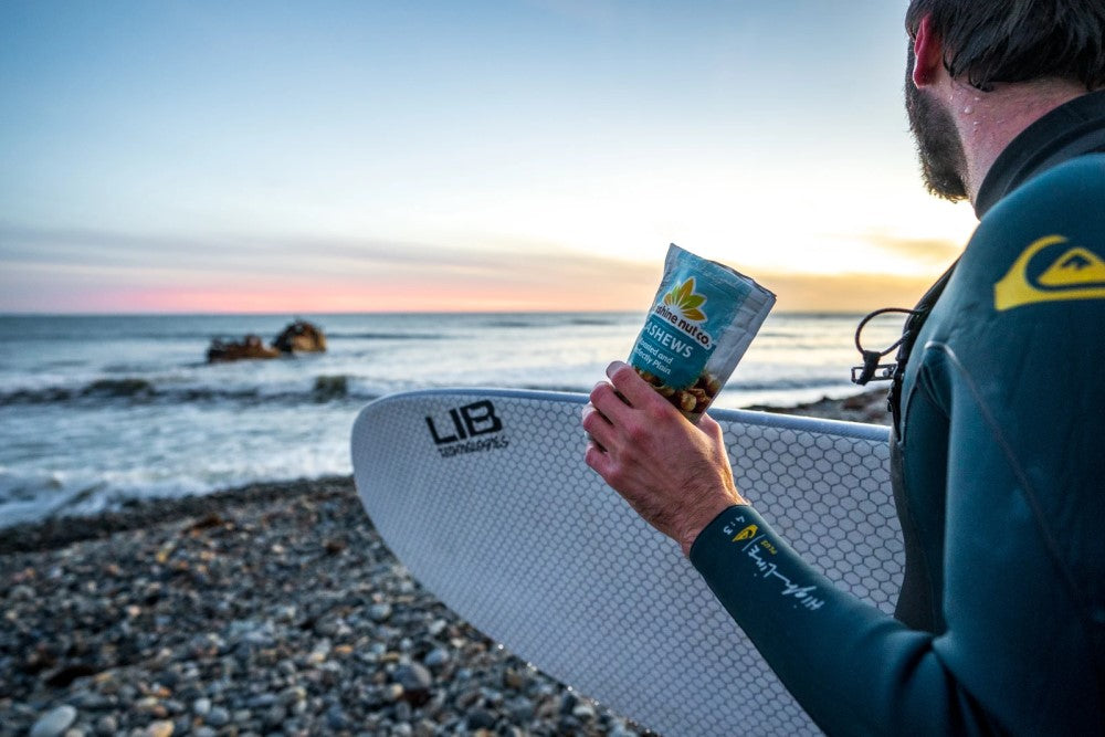 Surfer At The Beach In Quiksilver Holding Surfboard And Snacking On Roasted And Perfectly Plain Cashews From Sunshine Nut Co